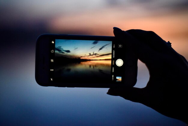 Photo cropped person photographing lake with mobile phone during sunset