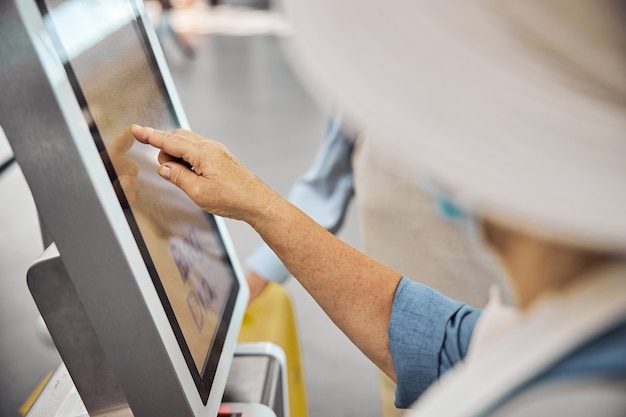 Cropped photo of an aged Caucasian lady checking in her luggage at a self-service kiosk