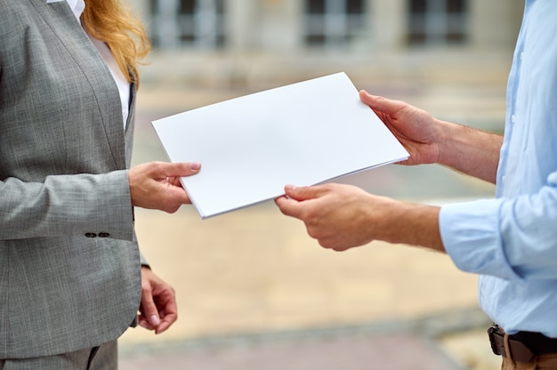 Photo cropped photo of a blonde stylish caucasian female inspector handing over building documentation to her male colleague