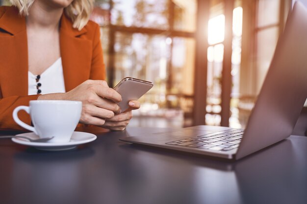 Обрезанное фото молодой блондинки-предпринимателя с мобильным телефоном, сидящей за столом
