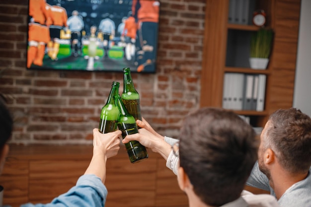 Cropped photo of a bottles of beer in men's hands watching a football game