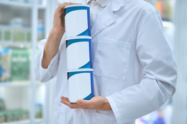 Обрезанное фото кавказского аптекаря, держащего в руках три баночки с новыми биологически активными добавками