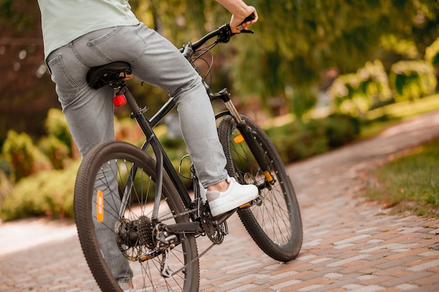 公園のタイル張りの自転車道に沿ってペダリングしている白人男性アスリートのトリミングされた写真