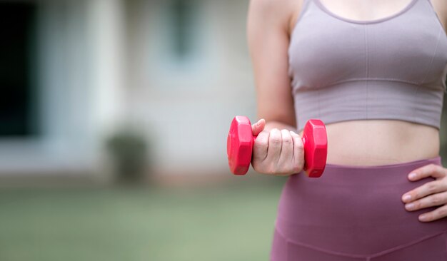 Cropped photo of caucasian woman workout with red dumbbell outdoors. Copy space.