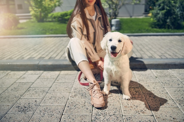 Foto ritagliata di una proprietaria di un cane femmina dai capelli scuri seduta sul marciapiede con il suo animale domestico