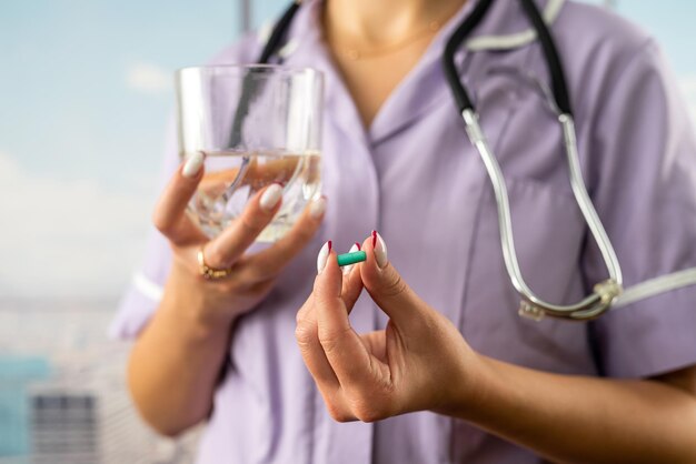 Foto foto ritagliata di una dottoressa che tiene pillola e bicchiere d'acqua in due mani in ospedale