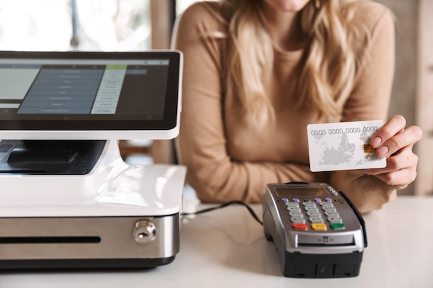 cropped photo of girl buyer in cafe holding credit card near terminal