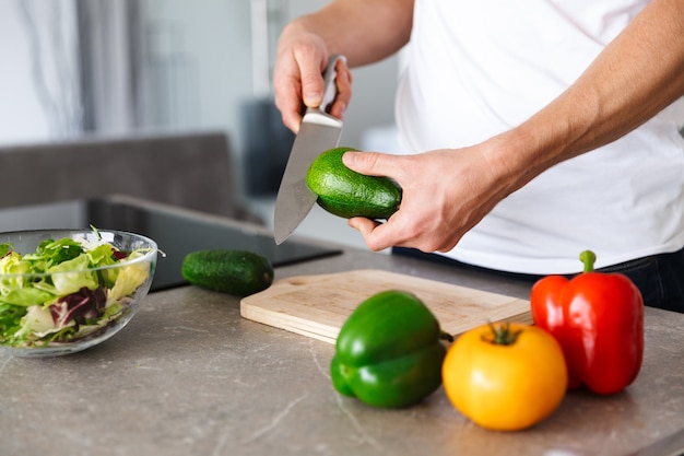 Cropped photo of a handsome young man at kitchen at home cooking vegetables make salad.