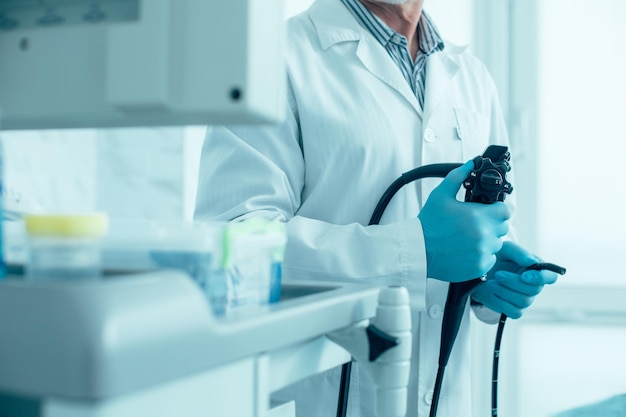 Photo cropped photo of a man in white coat and rubber gloves standing with a modern endoscope