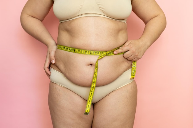 Cropped photo of naked fat and overweight woman tummy trying to lose weight Measuring by roulette tape belly Closeup