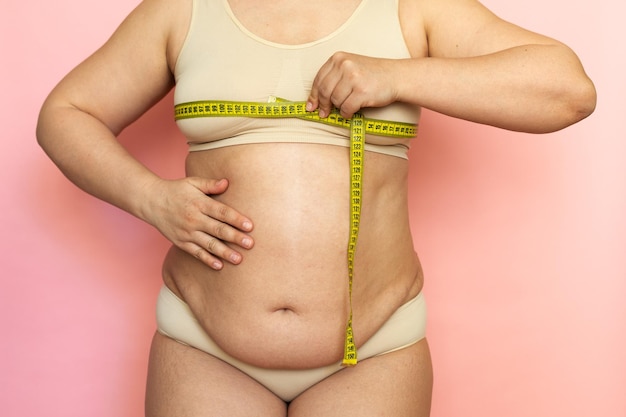 Cropped photo of naked overweight woman body holding and measuring by roulette tape her breast chest Unhealthy body