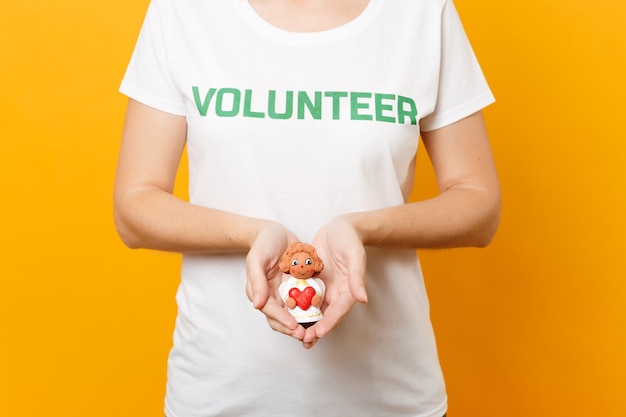 Фото Обрезанное фото женщины в белой футболке, написанной надписью зеленый титул волонтерского маленького ангела в ладонях, изолированных на желтом фоне. добровольная бесплатная помощь, концепция работы благотворительной благодати.