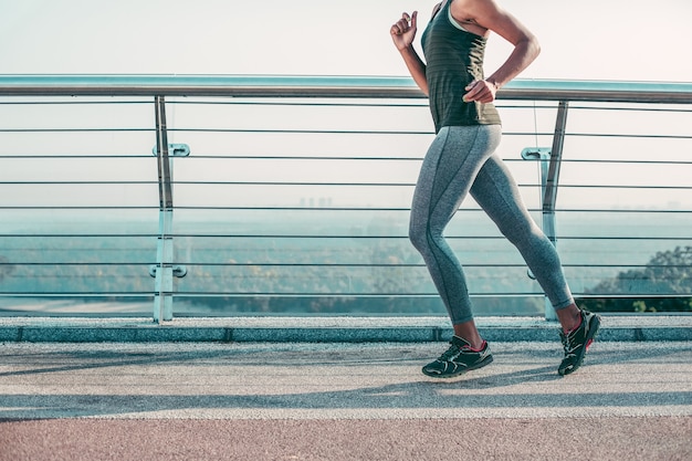 Cropped photo of a professional sportswoman in sneakers and tights running on the bridge. Website banner