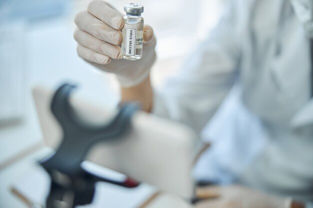 Cropped photo of a scientist holding a vial with a biopreparation in front of the cellphone camera