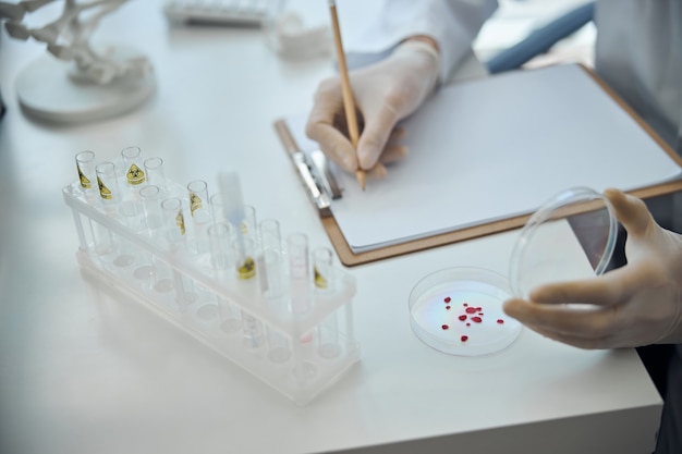 Cropped photo of a virologist in sterile gloves analyzing the blood sample on a tissue culture dish