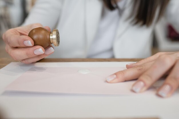 Cropped photo of wellgroomed hands of woman making white wax\
seal with stamp on white postcard envel