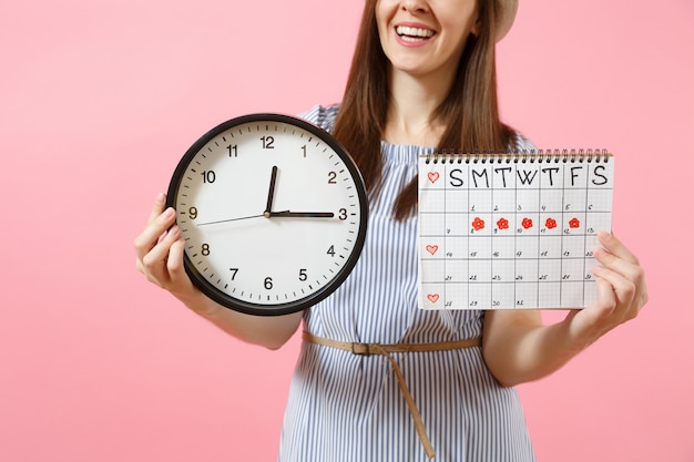 Foto ritagliata di donna in abito blu con orologio rotondo, calendario dei periodi per il controllo dei giorni delle mestruazioni isolati su sfondo rosa di tendenza. concetto medico, sanitario, ginecologico. copia spazio.