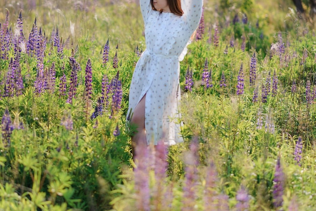 Photo cropped photo of a woman in a white dress in a field with lupins