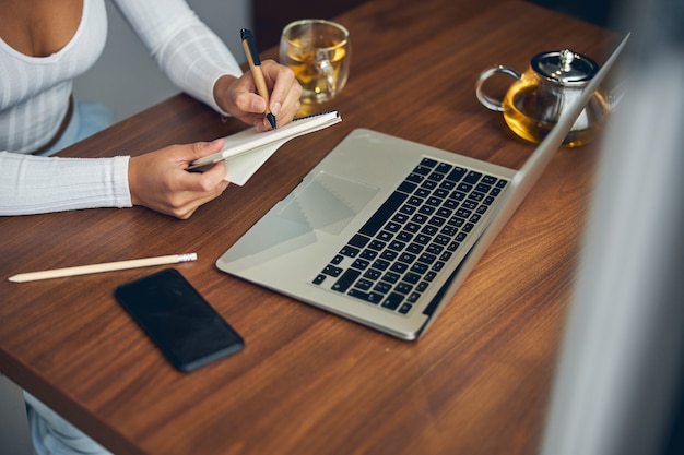 Cropped photo of woman in white sweater sitting and writing in notebook