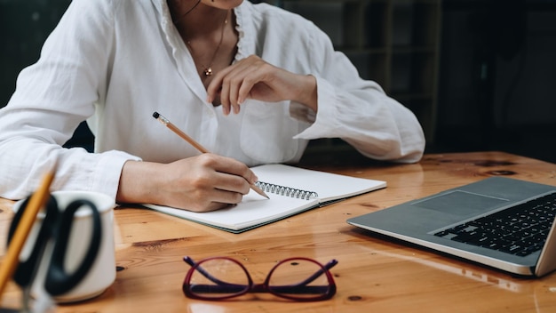 Cropped photo of woman writing making list taking notes in\
notepad working or learning on laptop indoors educational course or\
training seminar education online concept