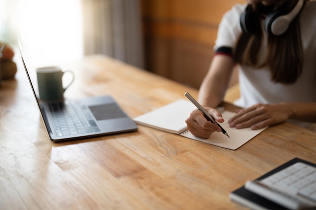 Cropped photo of woman writing making list taking notes in notepad working or learning on laptop indoors educational course or training seminar education online concept