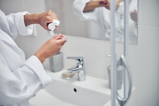 Cropped photo of the young female hands squeezing out the toothpaste from a plastic tube