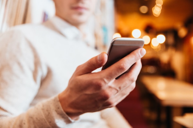 Cropped photo of young handsome man sitting in cafe while using mobile phone.