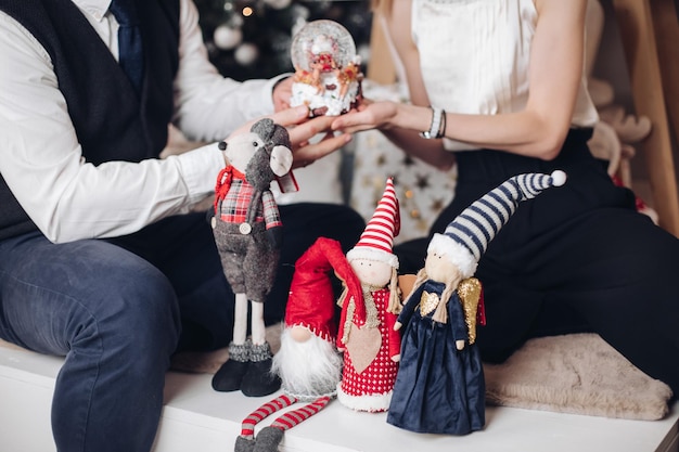 Cropped photo of young man and woman sitting at home with Christmas toys. New Year eve concept