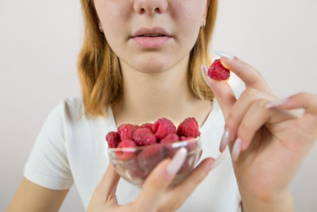 ガラスの鉢からラズベリーを食べている若い女性のカットされた写真