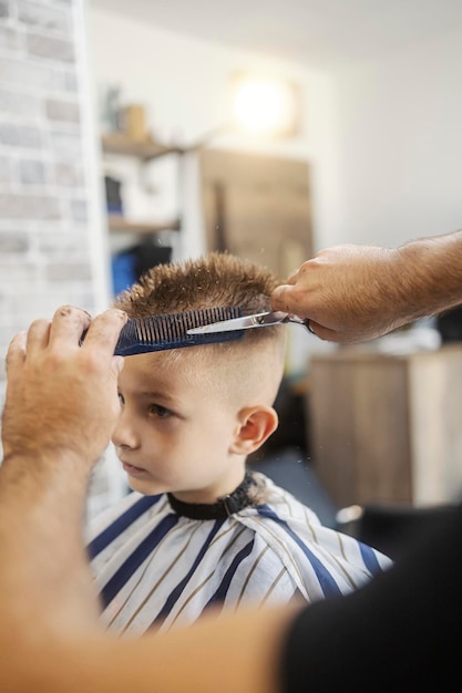 cropped picture of cute little boy in chair at barber shop having new haircut