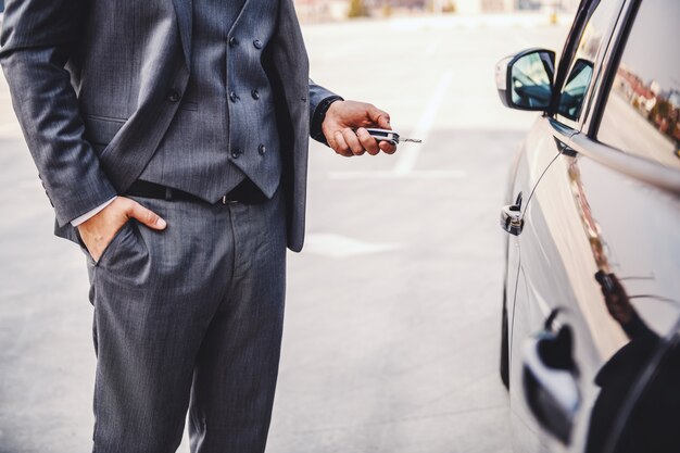 Foto ritagliata di elegante uomo d'affari in piedi accanto alla sua auto e tenendo le chiavi.