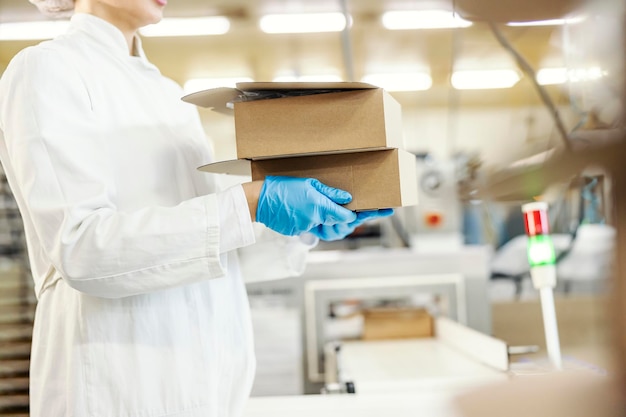 Обрезанное изображение работницы пищевой фабрики, руки которой несут коробки с выпечкой