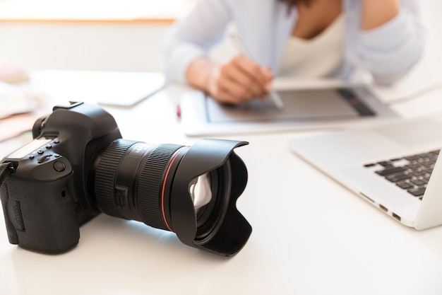 Photo cropped picture of photographer woman in office sitting at the table with camera working by graphic tablet retouching photos.