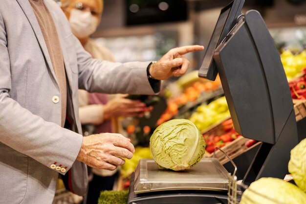 Cropped picture of a senior man measures cabbage on scales at the supermarket