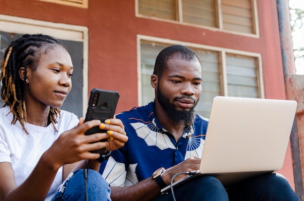 Обрезанное изображение двух африканцев, которые обмениваются файлами с ноутбука на мобильный телефон.