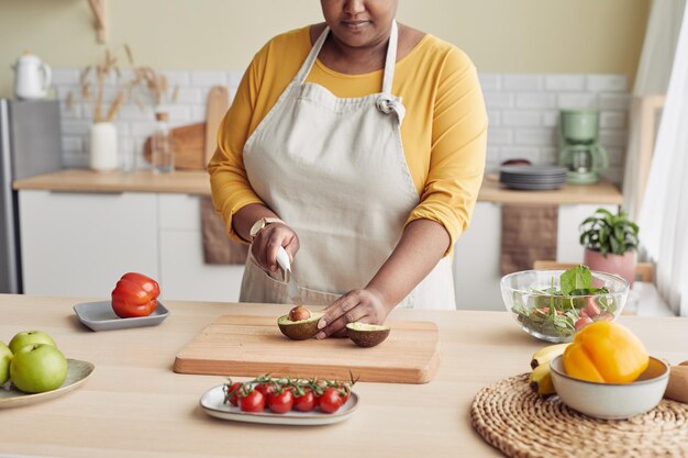 Ritratto ritagliato di donna nera che taglia l'avocado mentre cucina un pasto sano nello spazio della copia della cucina