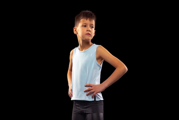 Cropped portrait of little boy running athlete posing in uniform isolated over black studio background