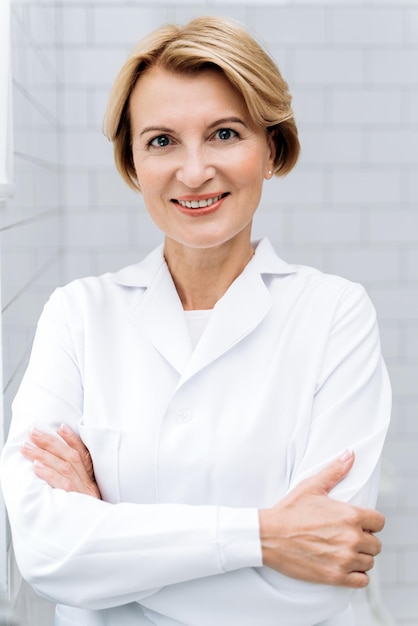 Cropped portrait of mature cosmetologist in white lab coat posing confidently and smiling Beauty and skin care concept