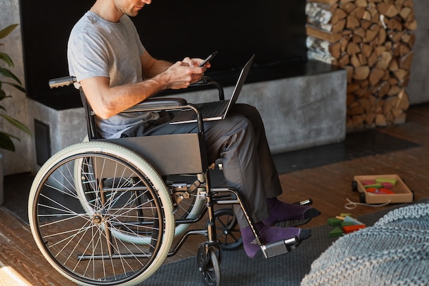 Cropped portrait of modern man with disability using laptop at home while sitting in wheelchair, copy space