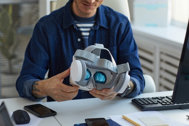 Cropped portrait of unrecognizable IT developer holding VR headset while working on augmenter reality applications, copy space