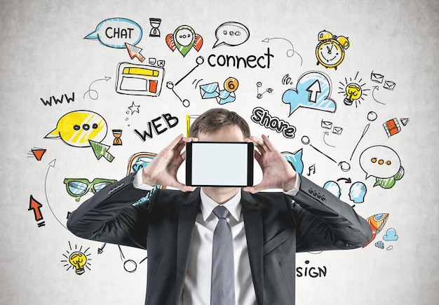 Photo cropped portrait of an unrecognizable young caucasian businessman with fair hair holding a blank tablet with copy space in front of his face. social media icons behind him. mock up