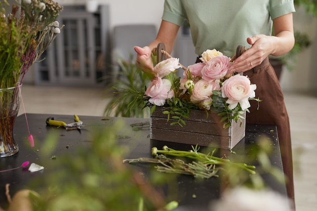 Ritagliato ritratto di giovane donna irriconoscibile che dispone composizione floreale con peonie rosa mentre lavora nel laboratorio di fioristi, copia spazio