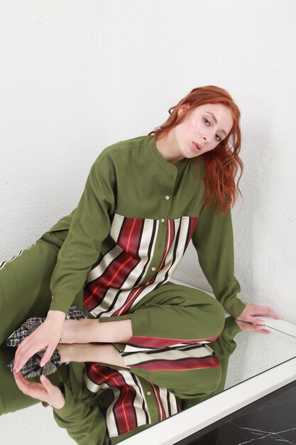 Photo cropped portrait of woman sitting on huge mirror in green stylish outfit against white wall studio