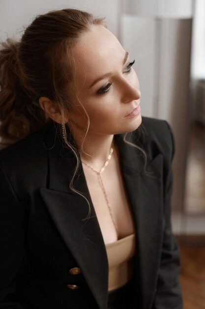 Cropped portrait of a young woman with gentle makeup wearing a\
fashionable blazer posing indoors.