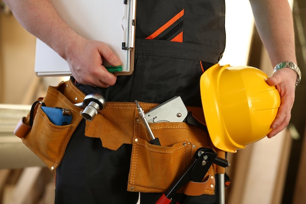 Cropped professional builder holding construction tools and helmet