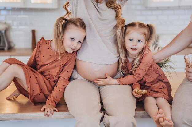 Cropped shoot of two little blonde girls with tails hugging their pregnant mothers belly