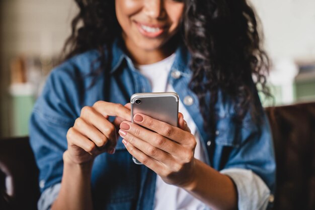 Foto foto ritagliata di una giovane donna afroamericana che usa lo smartphone a casa una donna afroamericana sorridente che usa uno smartphone a casa che manda messaggi o naviga sui social network mentre si rilassa sul divano