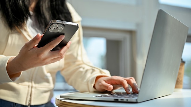 Cropped shot of an Asian woman using her smartphone while remote working at the cafe