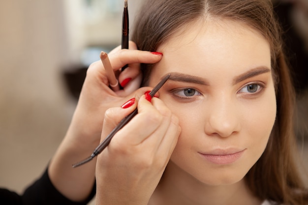 Cropped shot of a beautiful young woman smiling while professional make-up artist doing her eyebrows