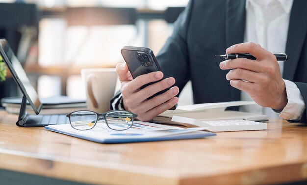 Photo cropped shot of businessman hand holding blank screeen smartphone while sitting at the table in modern office room, mock up blank screen for graphic design or product display.